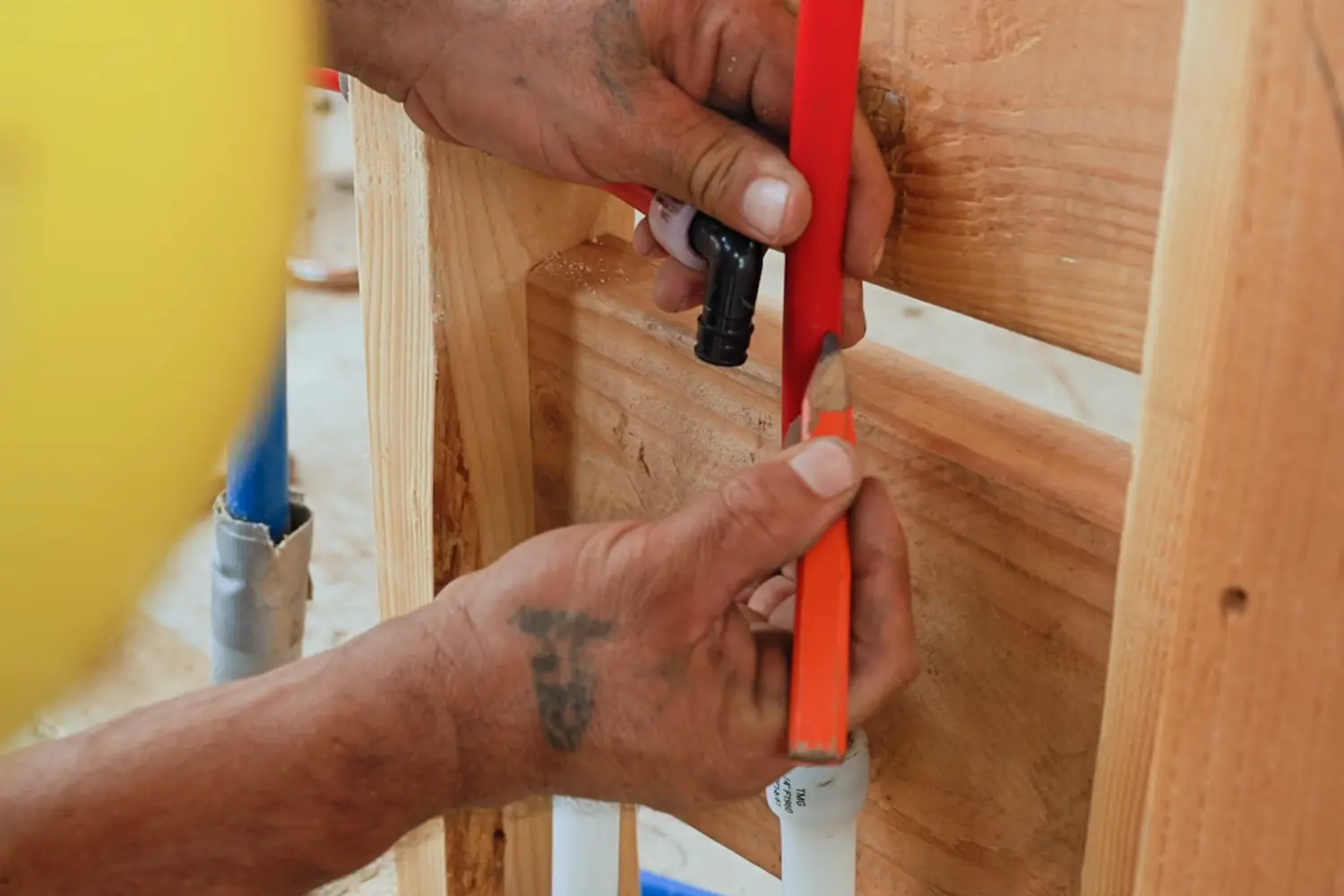 A plumber's hands crimping a red PEX supply line onto a fitting fixed to a stud